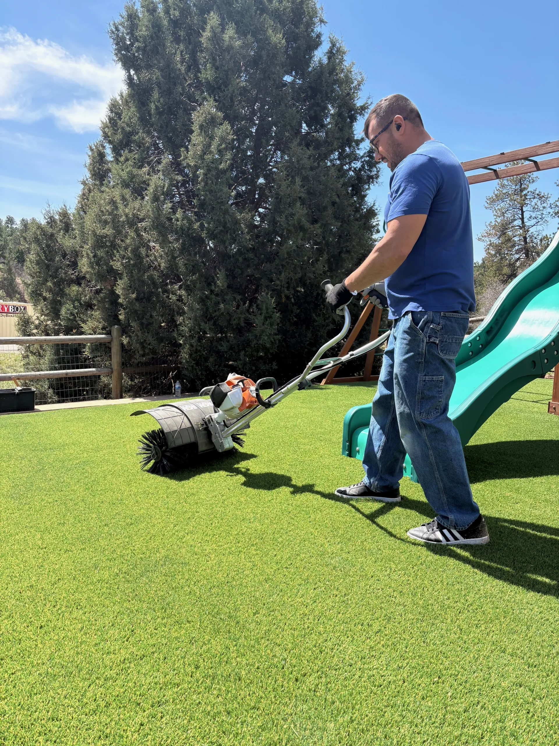 Turf Revival Pros technician grooming a backyard putting green with a commercial power broom in Colorado
